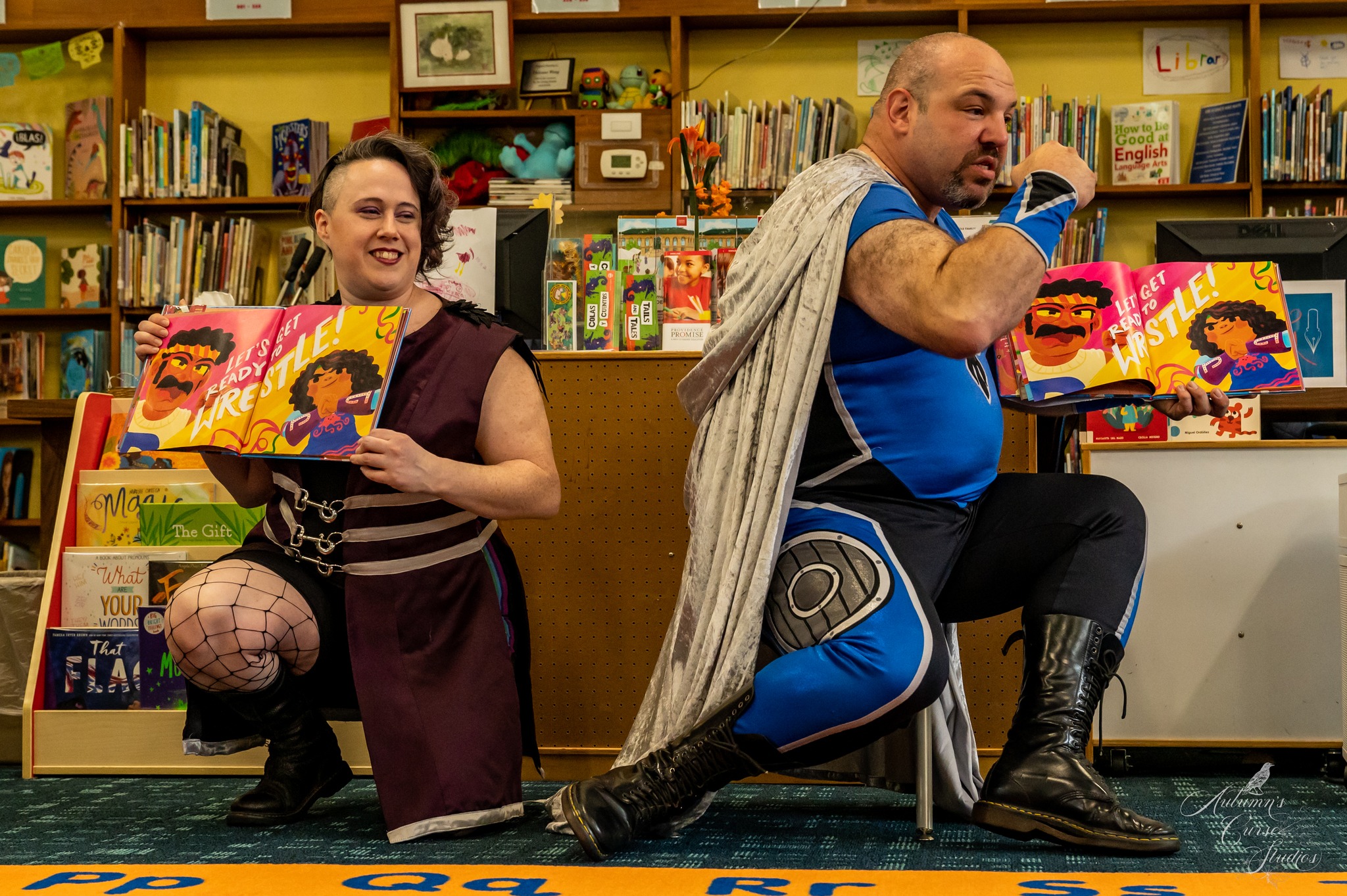 image: two people in superhero costumes reading picture books in a library