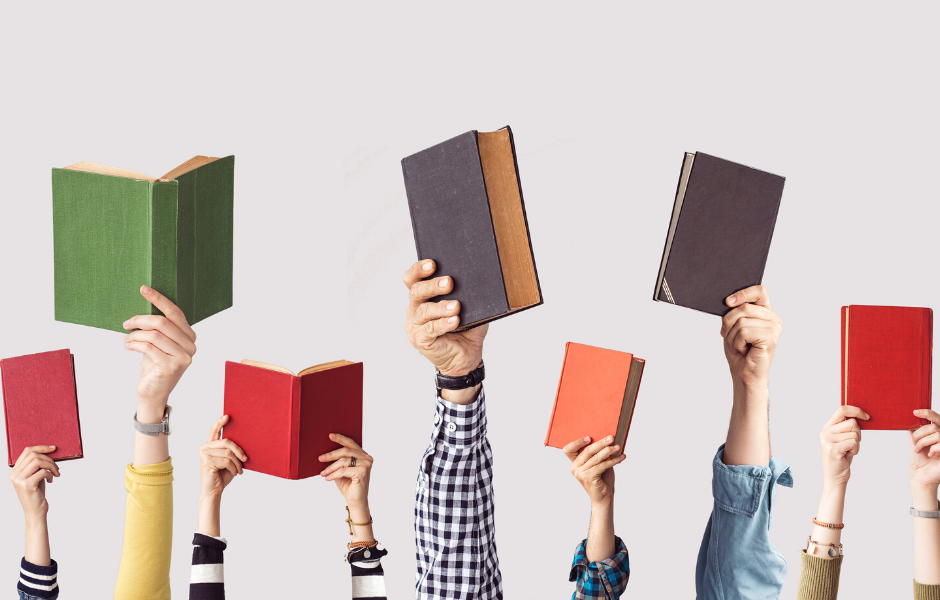 hands raising books of different colors up in the air